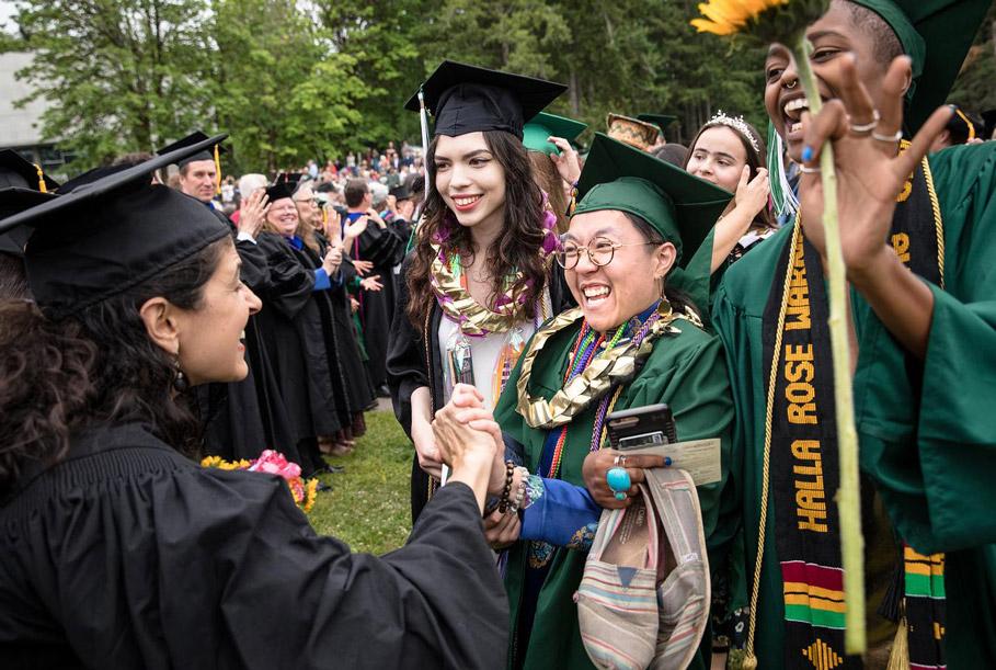 Evergreen graduates in green and black caps smiling and cheering one another on