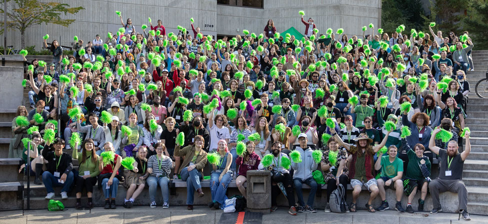 Hundreds of Evergreen Students seated in a group waving green pom poms.