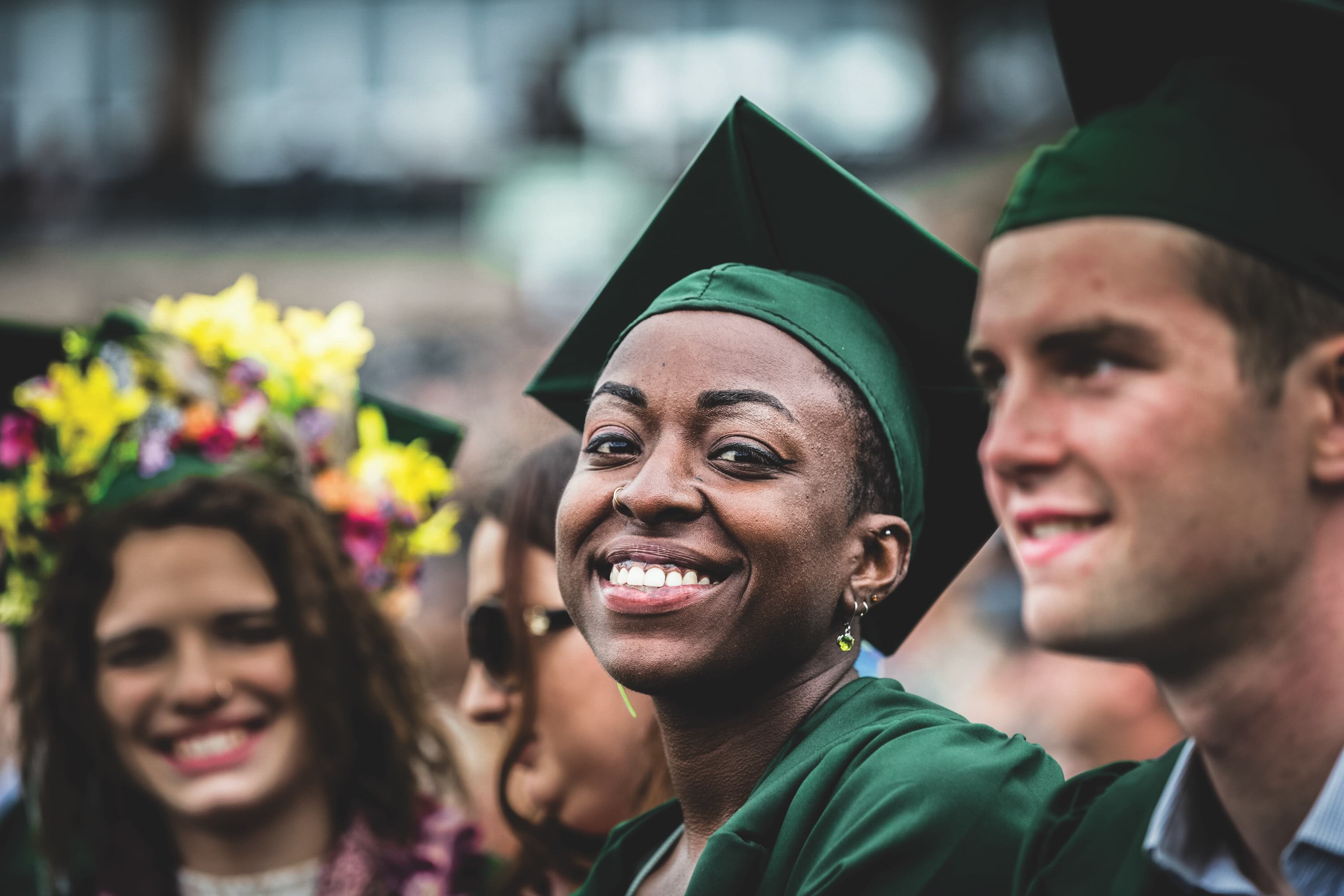 Three graduating students pictured wearing green cap and gown. 