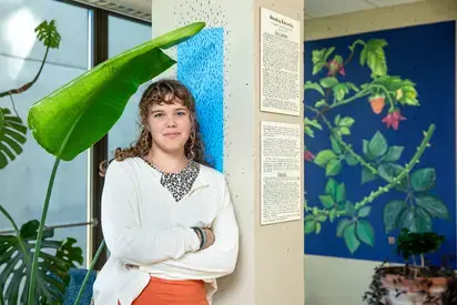 a student leaning against the wall, to their right is a mural they painted 