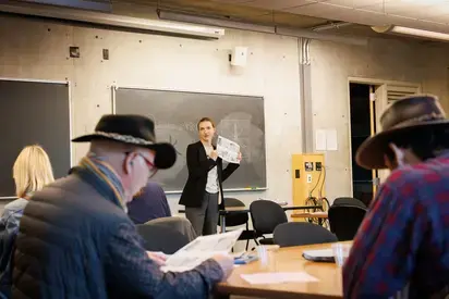 a group of people in a language workshop, someone is at the front of the classroom in front of a blackboard