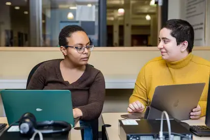 Two people using a laptop and a tablet