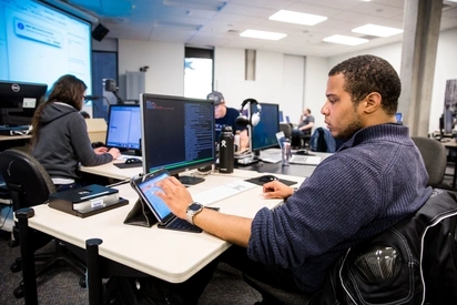 A student works simultaneously on a desktop computer and tablet to write code 