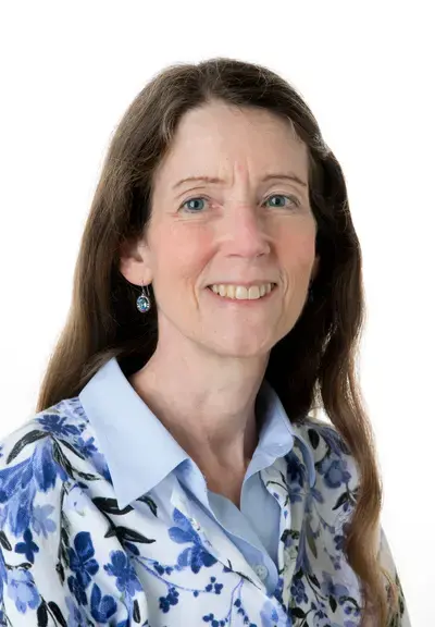 a white woman with long brown hair in a blue floral shirt smiling at the camera