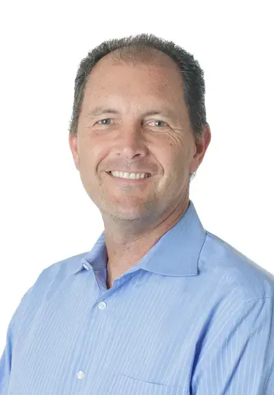 a white man in a light blue button down smiling at the camera