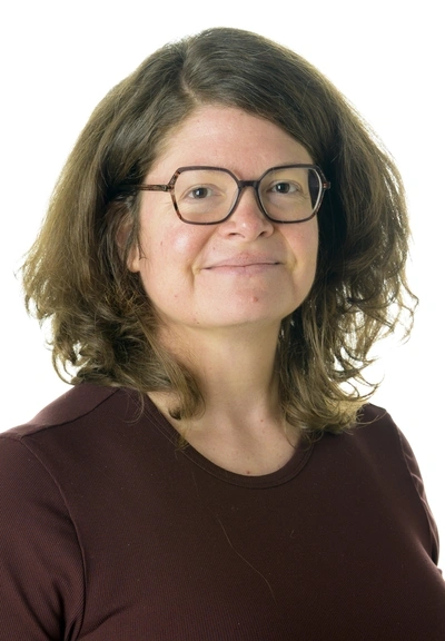 Person with sholder length brown hair wearing glasses and a rust red top