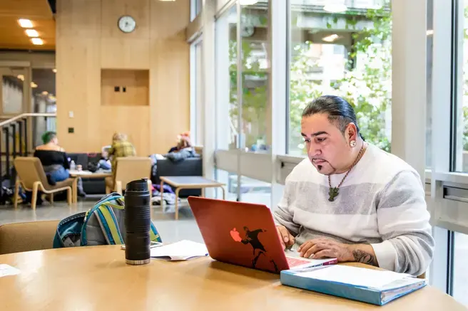 a man sits at a table with his laptop, notebook, and waterbottle