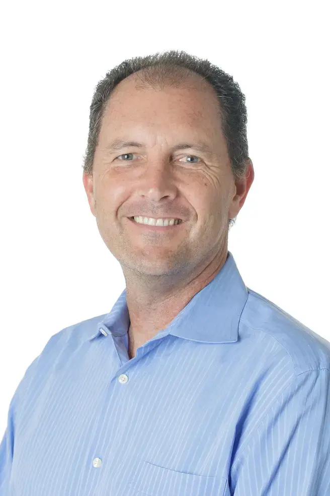 a white man in a light blue button down smiling at the camera