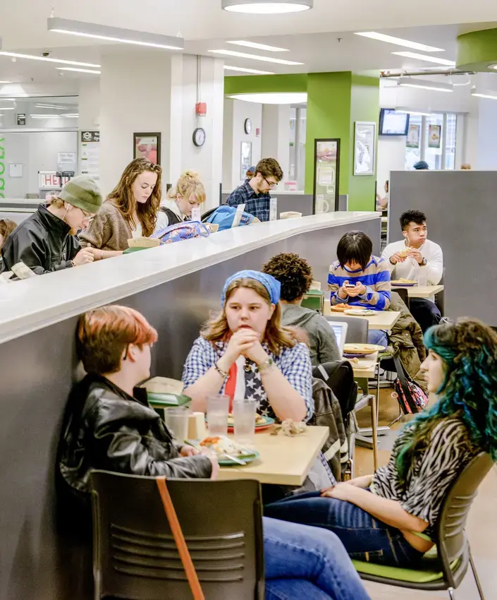 Groups of students eat luch and talk around tables in the greenery