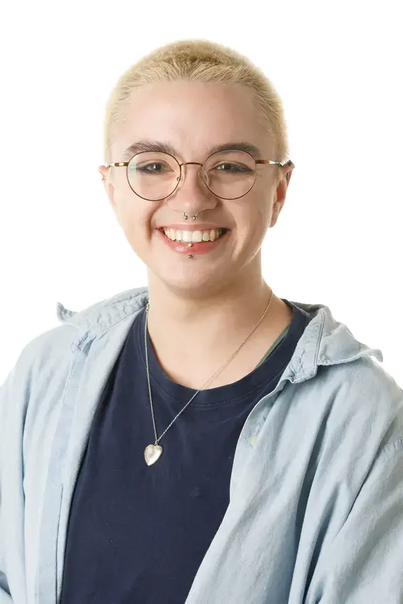 Person with short blond hair wearing glasses, a blue shirt and a silver necklace