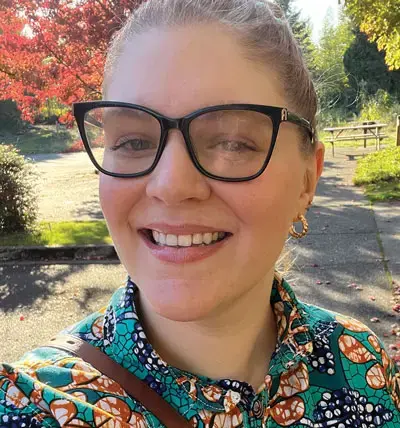 head and shoulders photo of a person wearing glasses, smiling, in an outdoor setting