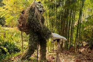 forest of bamboo and trees with sculpture of walking figure made of branches